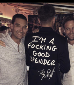 Matt Holt standing next to a person with the words "I'm a fucking good spender" on the back of a shirt